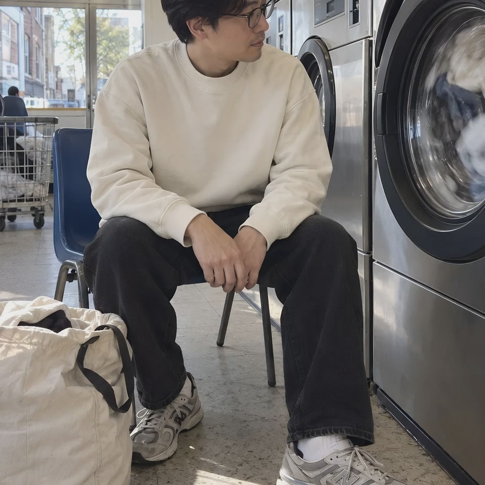 A man in the ENVY Crew Sweat waiting in a launderette while the drum turns